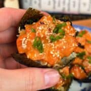 Close-up of spicy salmon sushi roll with sesame seeds and green onions.