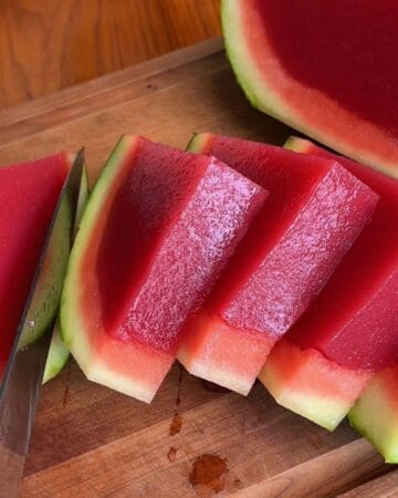 Juicy watermelon jello slices on a wooden cutting board with a knife.
