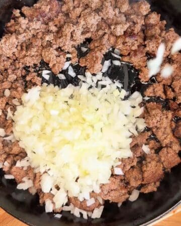 Ground beef and chopped onions cooking in a skillet for a crispy beef taco cones.