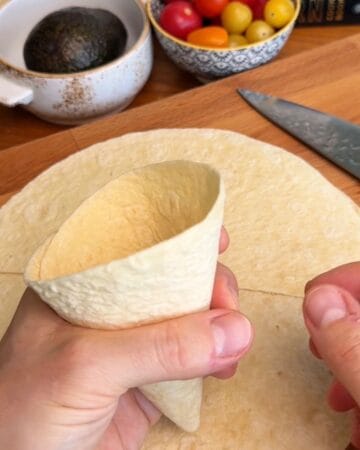 Person shaping a taco cone with hands on a wooden countertop.