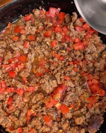 Cooked ground beef with diced tomatoes and onions in a skillet.