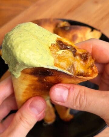 Close-up of a beef taco cone with green sauce and melted cheese.