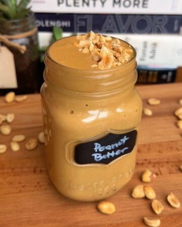 Smooth peanut butter topped with chopped peanuts in a glass jar.