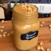 Creamy peanut butter in a glass jar with chopped peanuts on top.