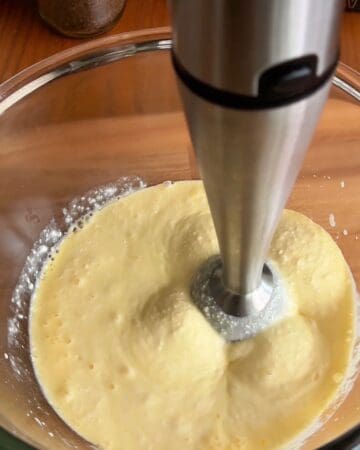 Egg mixture being blended with an immersion blender in a glass bowl.