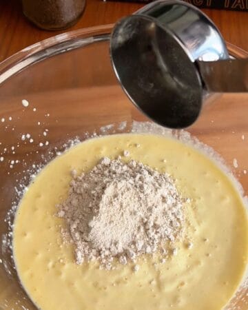 Pouring flour into a bowl of batter for baking.
