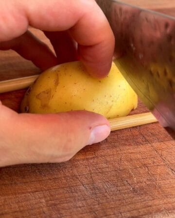 Hand slicing a potato on a wooden cutting board with a knife.
