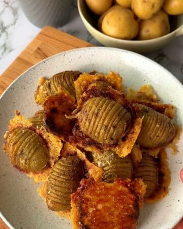 Crispy potatoes served on a white plate with a bowl of potatoes in the background.