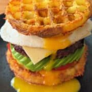 Delicious waffle burger with egg, avocado, tomato, and cheese, topped with crispy potato waffle buns