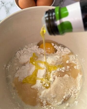 Pouring oil into flour and eggs in a mixing bowl for pancakes