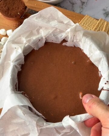 Rich homemade chocolate s'mores cheesecake in a baking pan with parchment paper.