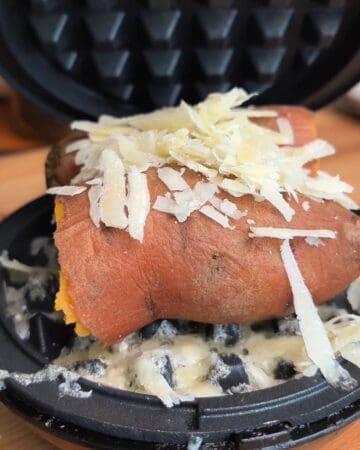 Sweet potato, covered in shredded cheese, in a waffle maker to be turned into a waffle.