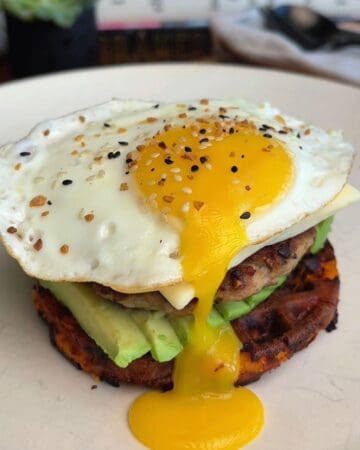 Close-up of a breakfast burger with fried egg, avocado, and grilled patty.