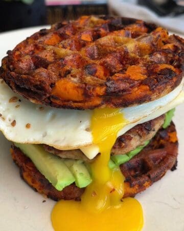 Savory breakfast sweet potato waffle burger with fried egg, avocado, and sausage patty.