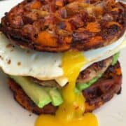 Delicious sweet potato waffle breakfast burger with fried egg, avocado, and crispy sausage patty.