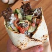 Beef kebab wrap with fresh cucumber, tomato, and creamy sauce in a toasted flatbread for a flavorful meal.