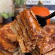 A fork lifting a piece of pumpkin swirl pancake with syrup, with a pumpkin in the background, perfect for fall breakfast.